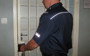 Umundurowany policjant zamykający kratę do pomieszczeń dla osób zatrzymanych.