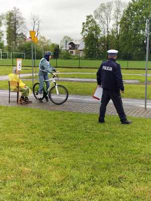 Dziecko na rowerze jadące po drodze. Obok umundurowany policjant.