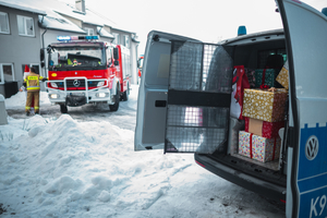 Parking przed budynkiem DPS w Sanoku. Radiowóz policyjny pełen prezentów. W tle samochód strażacki.