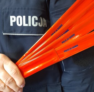 Umundurowany policjant trzymający w dłoni plik odblasków w kolorze czerwonym.