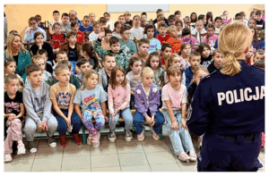 Umundurowani policjanci rozmawiają z grupą dzieci o bezpieczeństwie.