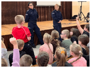 Umundurowani policjanci rozmawiają z grupą dzieci o bezpieczeństwie.
