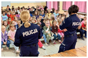 Umundurowani policjanci rozmawiają z grupą dzieci o bezpieczeństwie.