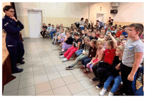 Umundurowani policjanci rozmawiają z grupą dzieci o bezpieczeństwie.