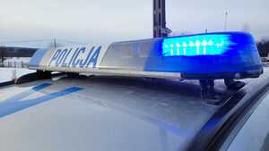 Belka z napisem POLICJA na dachu radiowozu. W tle zaśnieżone pola.