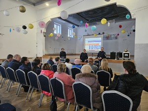 Policjanci przeprowadzający debatę społeczną poświęconą bezpieczeństwu seniorów. Na zdjęciu widać prelegentów oraz uczestników debaty siedzących na krzesłach.