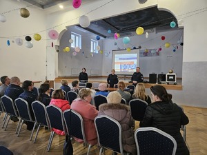 Policjanci przeprowadzający debatę społeczną poświęconą bezpieczeństwu seniorów. Na zdjęciu widać prelegentów oraz uczestników debaty siedzących na krzesłach.