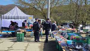Policjanci patrolujący targowisko. W tle widać sprzedawców i kupujących oraz towar, którym handlują.