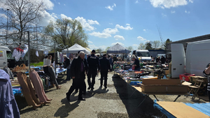 Policjanci patrolujący targowisko. W tle widać sprzedawców i kupujących oraz towar, którym handlują.