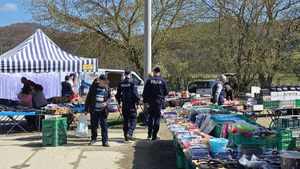 Policjanci patrolujący targowisko. W tle widać sprzedawców i kupujących oraz towar, którym handlują.