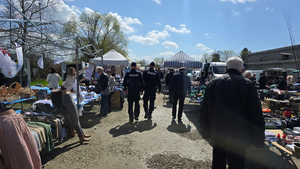 Policjanci patrolujący targowisko. W tle widać sprzedawców i kupujących oraz towar, którym handlują.