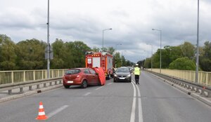 Zdjęcie z miejsca zdarzenia. Widać czerwony samochód osobowy znajdujący się przy barierach ochronnych. Tuż za nim stojący oznakowany radiowóz.