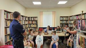 Dzielnicowy znajdujący się w bibliotece. Policjant czyta książkę grupie dzieci.