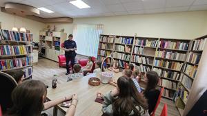 Dzielnicowy znajdujący się w bibliotece. Policjant czyta książkę grupie dzieci.