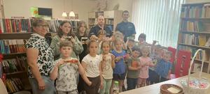 Dzielnicowy znajdujący się w bibliotece. Policjant czyta książkę grupie dzieci.