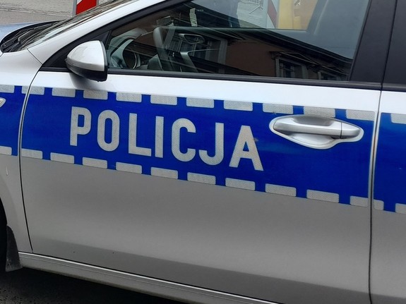 Bok radiowozu oznakowanego, z widocznymi drzwiami bocznymi. Na drzwiach nalepka z napisem POLICJA