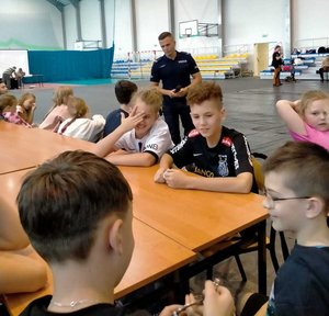 Dzielnicowy przeprowadzający pogadankę profilaktyczną z dziećmi, które uczestniczą w półkoloniach.