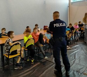 Dzielnicowy przeprowadzający pogadankę profilaktyczną z dziećmi, które uczestniczą w półkoloniach.
