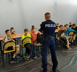 Dzielnicowy przeprowadzający pogadankę profilaktyczną z dziećmi, które uczestniczą w półkoloniach.