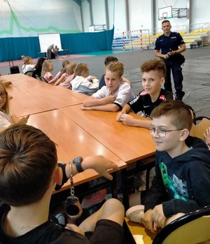 Dzielnicowy przeprowadzający pogadankę profilaktyczną z dziećmi, które uczestniczą w półkoloniach.