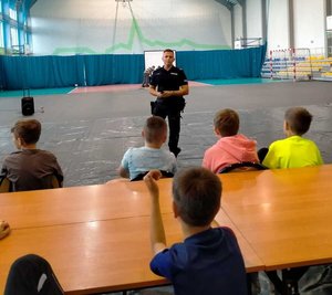 Dzielnicowy przeprowadzający pogadankę profilaktyczną z dziećmi, które uczestniczą w półkoloniach.