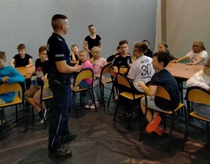 Dzielnicowy przeprowadzający pogadankę profilaktyczną z dziećmi, które uczestniczą w półkoloniach.