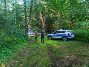 Czynności wykonywane prze policjantów wspólnie ze strażnikami leśnymi. Radiowóz zaparkowany w lesie.