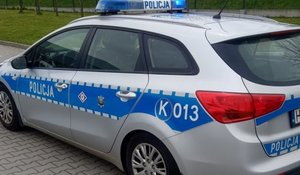 Oznakowany radiowóz stojący bokiem. W tle zielony trawnik.