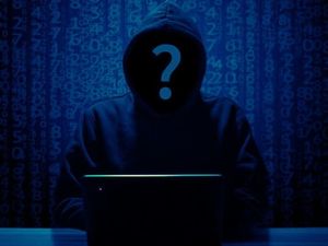 Ciemna postać człowieka na ciemnym tle. Ubrany w bluzę z kapturem. Zamiast twarzy widnieje znak zapytania.