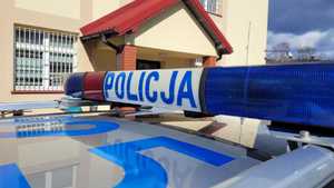 Belka z napisem POLICJA na dachu radiowozu. W tle żółty budynek.