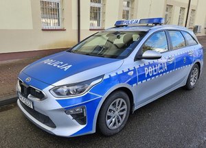 Oznakowany radiowóz stojący przy budynku z żółtymi ścianami.