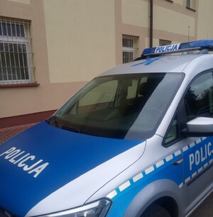 Radiowóz oznakowany zaparkowany przy budynku. Pogoda deszczowa.