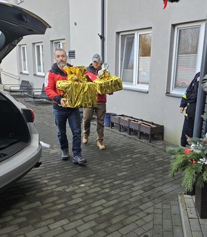 Umundurowani policjanci noszący paczki mikołajowe dla podopiecznych DPSu.  Policjanci biorą paczki z samochodu i wnoszą do budynku, w którym odbędzie się wręczanie prezentów autorom listów.