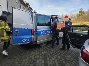 Umundurowani policjanci noszący paczki mikołajowe dla podopiecznych DPSu.  Policjanci biorą paczki z samochodu i wnoszą do budynku, w którym odbędzie się wręczanie prezentów autorom listów.