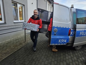Umundurowani policjanci noszący paczki mikołajowe dla podopiecznych DPSu.  Policjanci biorą paczki z samochodu i wnoszą do budynku, w którym odbędzie się wręczanie prezentów autorom listów.