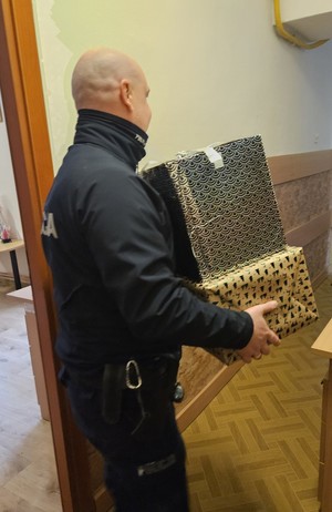 Umundurowani policjanci noszący paczki mikołajowe dla podopiecznych DPSu.  Policjanci biorą paczki z samochodu i wnoszą do budynku, w którym odbędzie się wręczanie prezentów autorom listów.