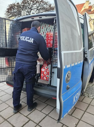 Umundurowani policjanci noszący paczki mikołajowe dla podopiecznych DPSu.  Policjanci biorą paczki z samochodu i wnoszą do budynku, w którym odbędzie się wręczanie prezentów autorom listów.