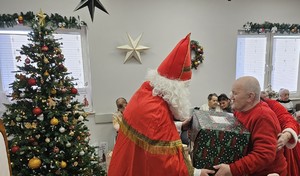 Umundurowani policjanci noszący paczki mikołajowe dla podopiecznych DPSu.  Policjanci biorą paczki z samochodu i wnoszą do budynku, w którym odbędzie się wręczanie prezentów autorom listów.