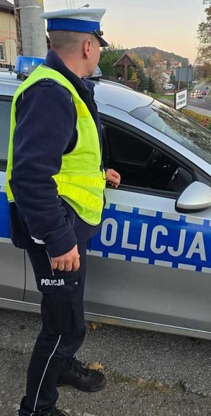 Umundurowany policjant stojący po prawej stronie radiowozu oznakowanego.