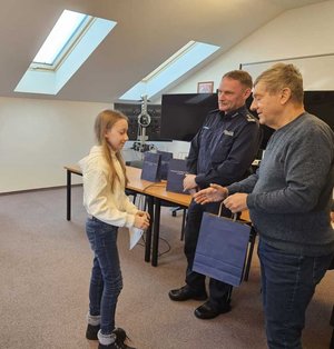 Rozstrzygnięcie konkursu pt. "Bezpieczne Wakacje 2025". Na zdjęciu widać osoby, które oceniały prace uczestników, osoby wręczające nagrody oraz nagrodzone dzieci razem z opiekunami.