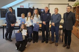 Rozstrzygnięcie konkursu pt. "Bezpieczne Wakacje 2025". Na zdjęciu widać osoby, które oceniały prace uczestników, osoby wręczające nagrody oraz nagrodzone dzieci razem z opiekunami.