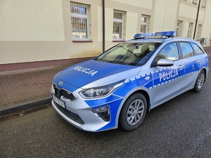 Na zdjęciu radiowóz oznakowany. Samochód zaparkowany jest wzdłuż budynku o żółtych ścianach.