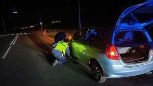 Umundurowany policjant pomagający w wymianie niesprawnego koła w samochodzie.