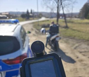 Na zdjęciu miejsce kontroli drogowej. Widać fragment urządzenia do mierzenia prędkości, motocykl oraz część radiowozu oznakowanego.
