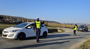 Samochód osobowy koloru białego. Przy oknie kierowcy stoi umundurowany policjant, przeprowadzający badanie na stan trzeźwości.