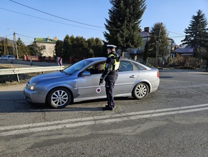 Samochód osobowy koloru szarego. Przy oknie kierowcy stoi umundurowany policjant, przeprowadzający badanie na stan trzeźwości.