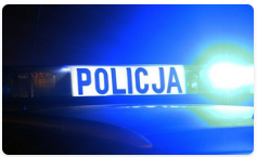 Belka z napisem POLICJA umieszczona na dachu radiowozu. Widoczne włączone niebieskie sygnały uprzywilejowania. Pora nocna, ciemno.